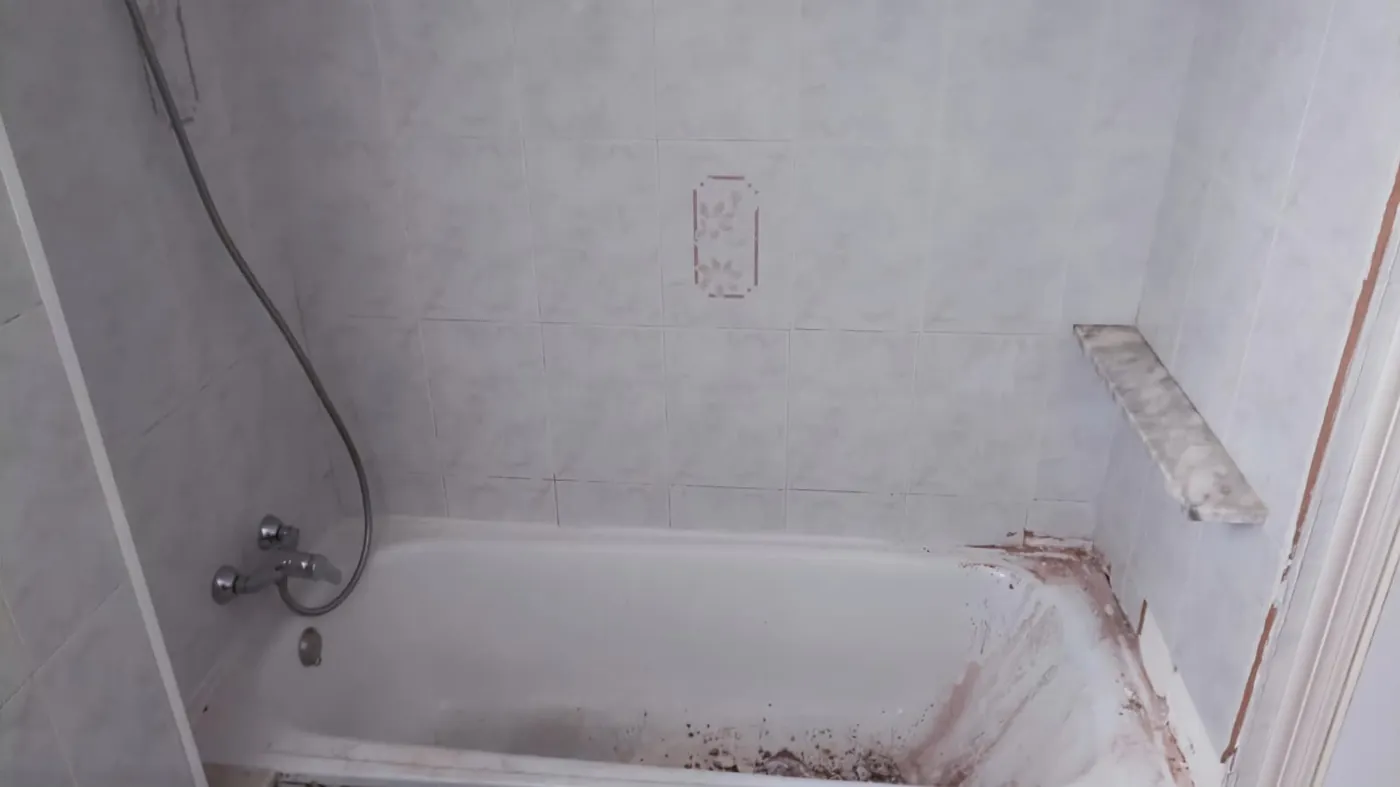 Antes: bañera de chapa esmaltada con óxido y moho en el borde, alicatado blanco con cenefa floral y grifería de bañera cromada