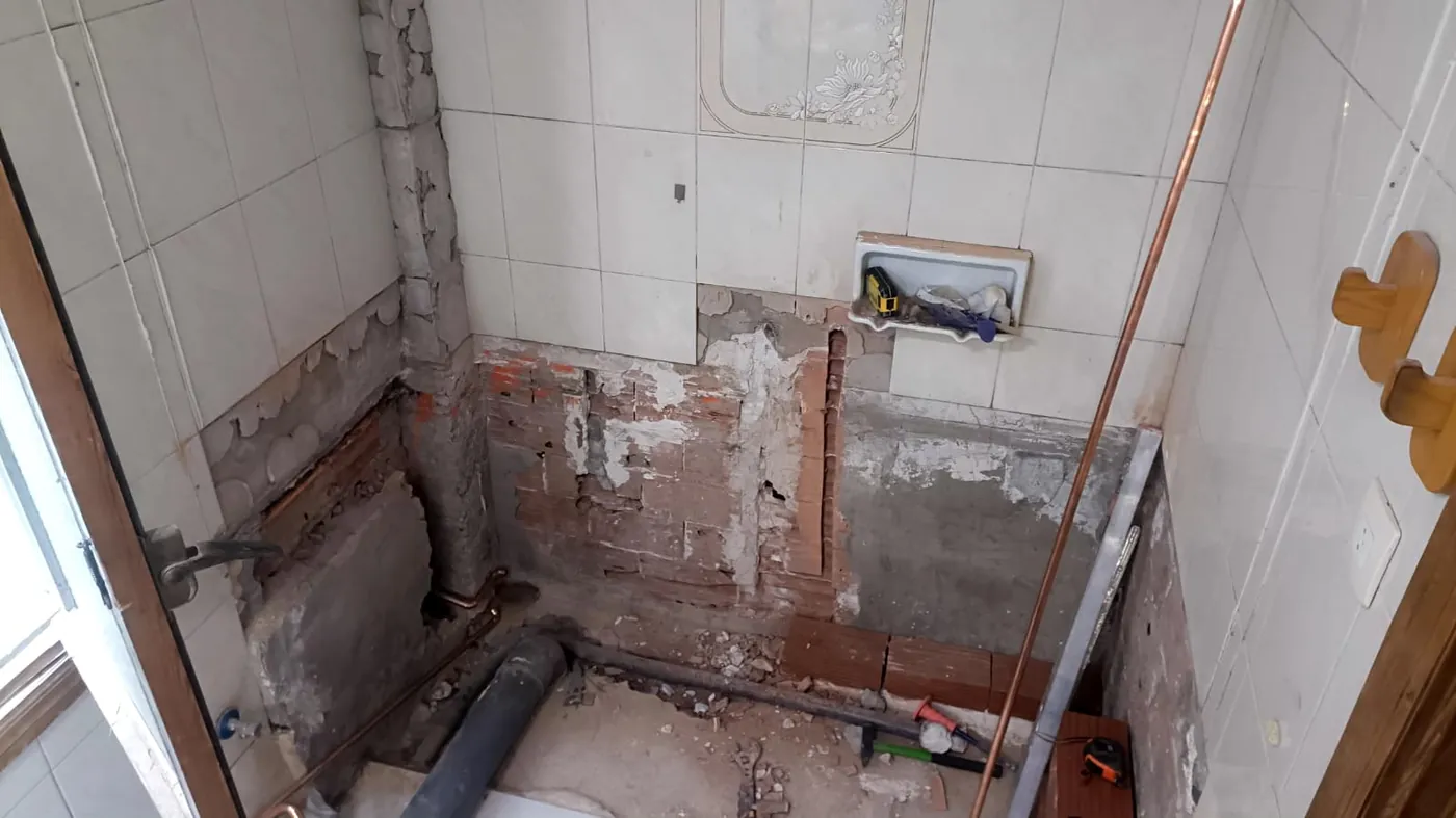Baño en obra en Alicante con la bañera ya retirada, la pared picada hasta el ladrillo, tubería de cobre nueva vista y el desagüe preparado
