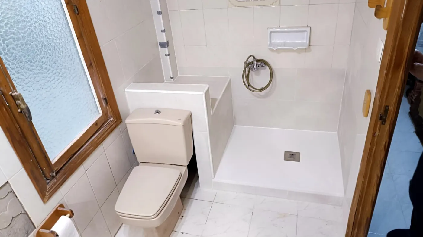 El mismo baño terminado: plato de ducha blanco de baja altura, murete de mármol que separa el inodoro y alicatado original conservado