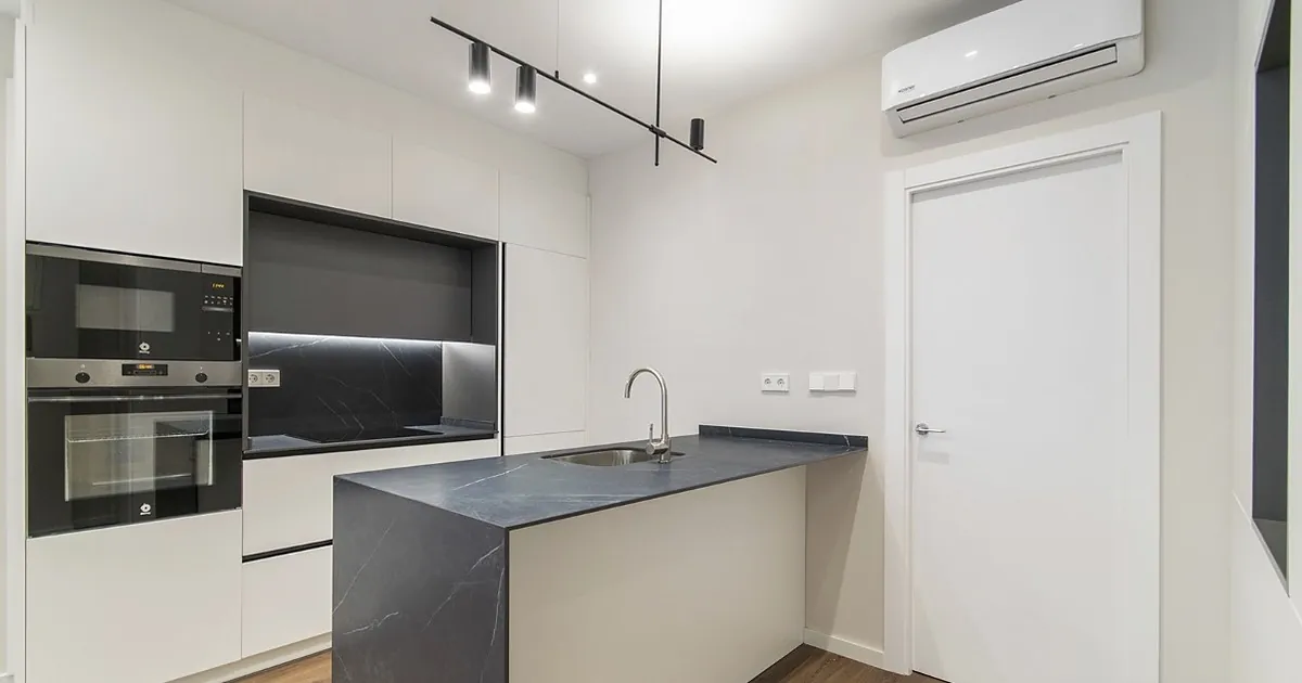 Cocina blanca sin tiradores con encimera negra y península en una vivienda de Alicante
