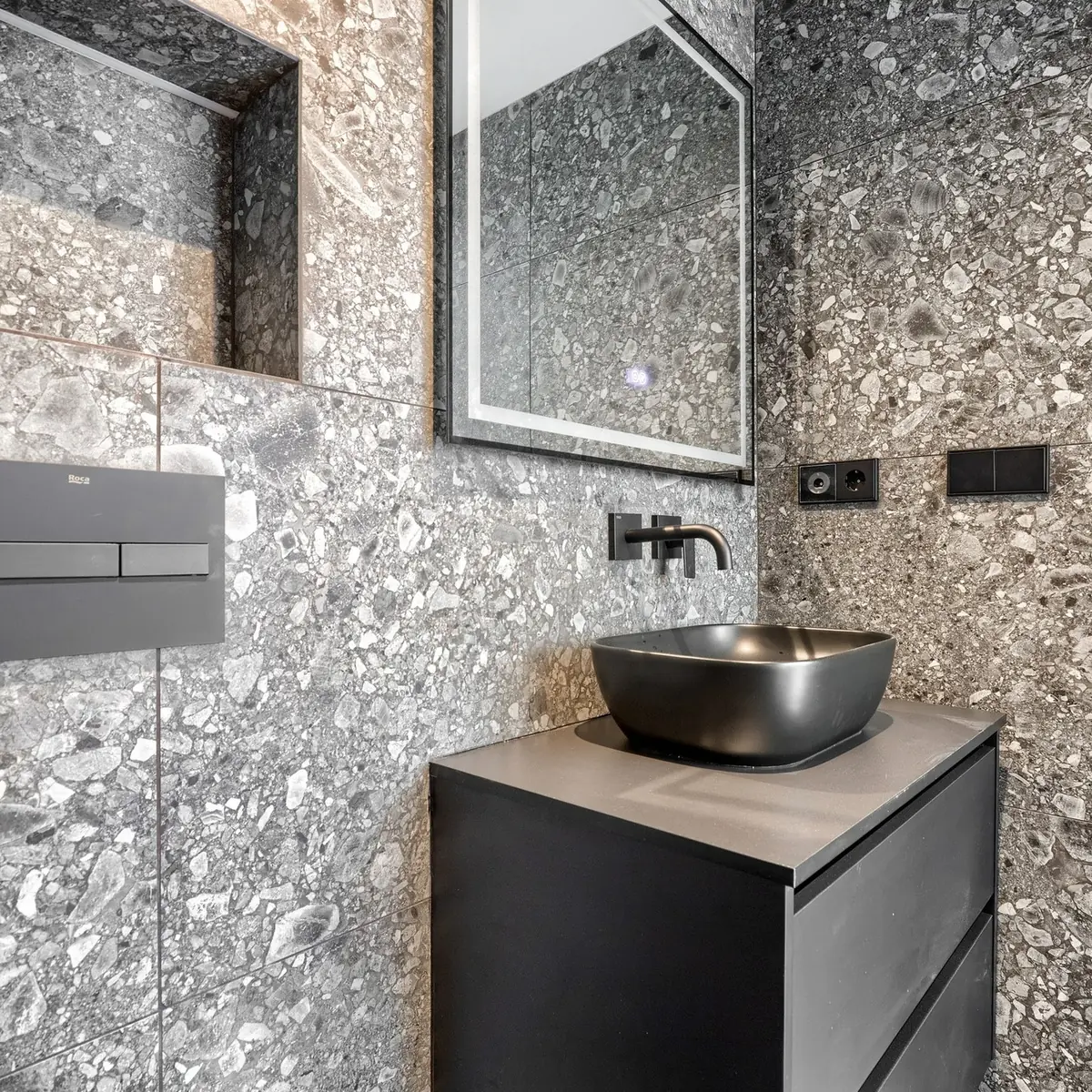 Lavabo sobre encimera en negro mate con grifería empotrada y revestimiento de terrazo gris